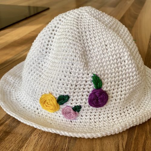 A knitted sunhead with embroidered flowers on a wooden surface