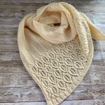 Delicate lace shawl hand-knit with white Drops Karisma yarn, featuring an intricate leaf motif. The openwork knit structure creates a light, airy fabric with fine stitch detail, ideal for showcasing lace patterns in shawls and scarves.