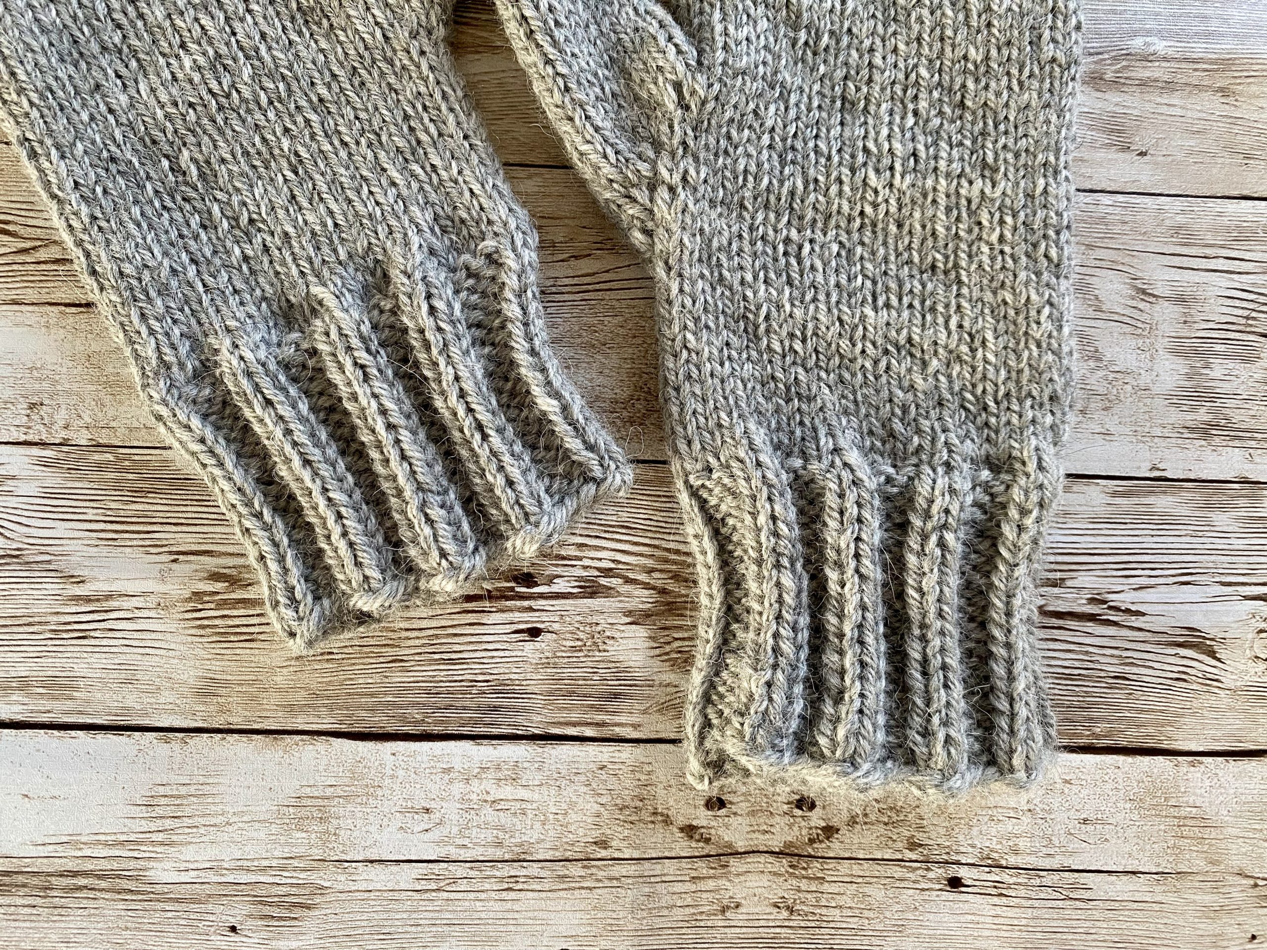 Close-up of light gray mittens featuring a 2x2 ribbing pattern, displayed on a wooden surface.