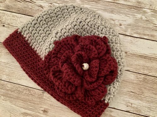 A knitted hat with a knitted flower and a pearl on a wooden surface