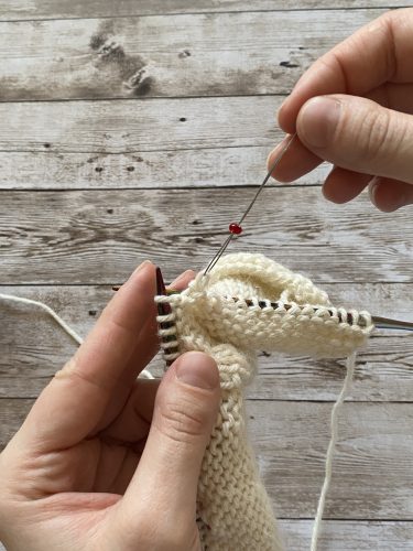 Step-by-step tutorial image demonstrating one of three techniques for threading beads onto yarn for knitting: using a hook, dental floss or thread, or pre-threading. The image shows the tools, materials, and process clearly to guide the viewer through the technique.