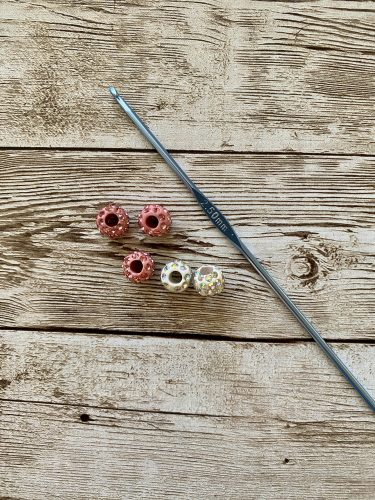 Step-by-step tutorial image demonstrating one of three techniques for threading beads onto yarn for knitting: using a hook, dental floss or thread, or pre-threading. The image shows the tools, materials, and process clearly to guide the viewer through the technique.