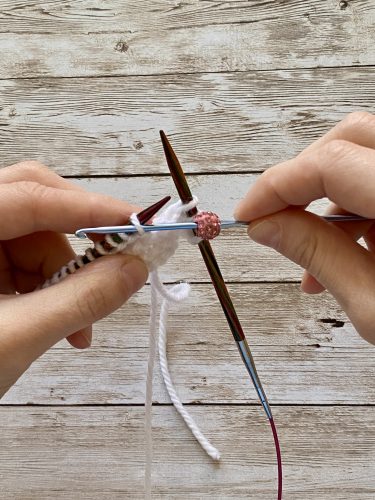 Step-by-step tutorial image demonstrating one of three techniques for threading beads onto yarn for knitting: using a hook, dental floss or thread, or pre-threading. The image shows the tools, materials, and process clearly to guide the viewer through the technique.