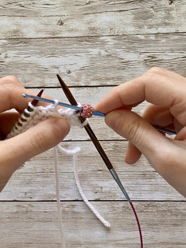 Step-by-step tutorial image demonstrating one of three techniques for threading beads onto yarn for knitting: using a hook, dental floss or thread, or pre-threading. The image shows the tools, materials, and process clearly to guide the viewer through the technique.