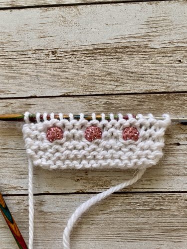 Step-by-step tutorial image demonstrating one of three techniques for threading beads onto yarn for knitting: using a hook, dental floss or thread, or pre-threading. The image shows the tools, materials, and process clearly to guide the viewer through the technique.