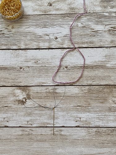 Step-by-step tutorial image demonstrating one of three techniques for threading beads onto yarn for knitting: using a hook, dental floss or thread, or pre-threading. The image shows the tools, materials, and process clearly to guide the viewer through the technique.