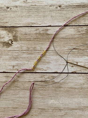Step-by-step tutorial image demonstrating one of three techniques for threading beads onto yarn for knitting: using a hook, dental floss or thread, or pre-threading. The image shows the tools, materials, and process clearly to guide the viewer through the technique.