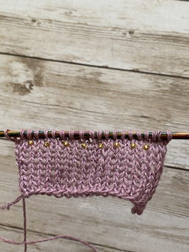 Step-by-step tutorial image demonstrating one of three techniques for threading beads onto yarn for knitting: using a hook, dental floss or thread, or pre-threading. The image shows the tools, materials, and process clearly to guide the viewer through the technique.