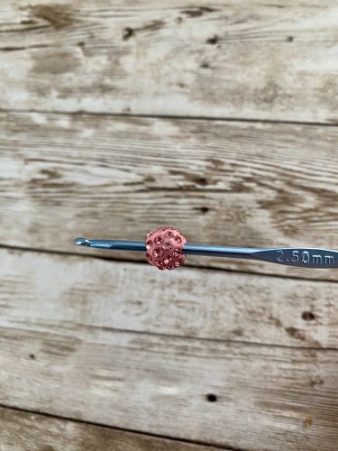 Step-by-step tutorial image demonstrating one of three techniques for threading beads onto yarn for knitting: using a hook, dental floss or thread, or pre-threading. The image shows the tools, materials, and process clearly to guide the viewer through the technique.