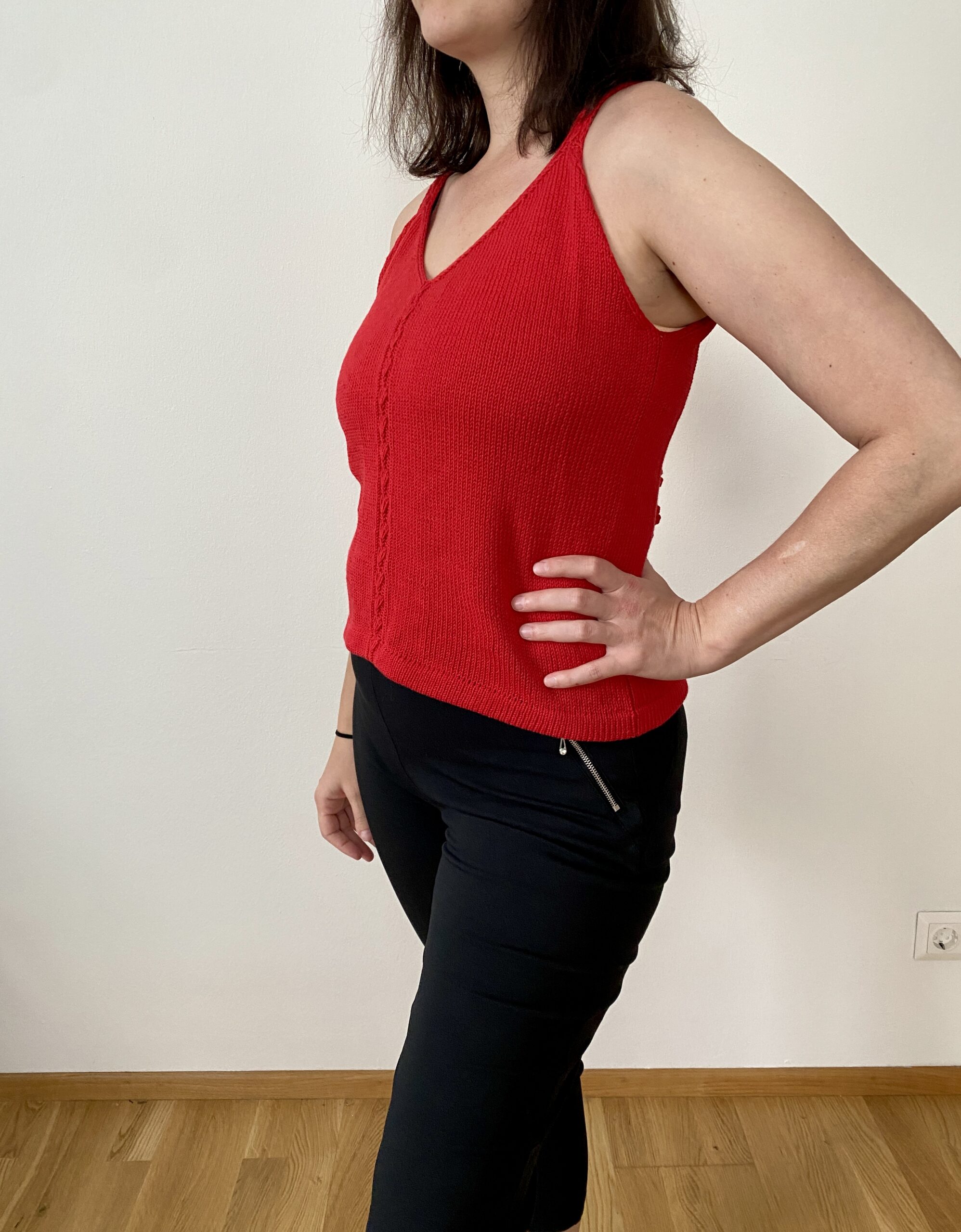A side view of the Ginkgo Biloba Top, worn by a woman. The vibrant red top showcases its fitted silhouette, V-neckline, and central lace detail, paired with black pants for a modern and sleek outfit.
