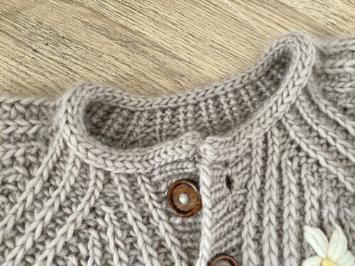 A detailed view of the neckline of the Fluffy Daisy Cardigan, highlighting the ribbed texture and a wooden button closure.