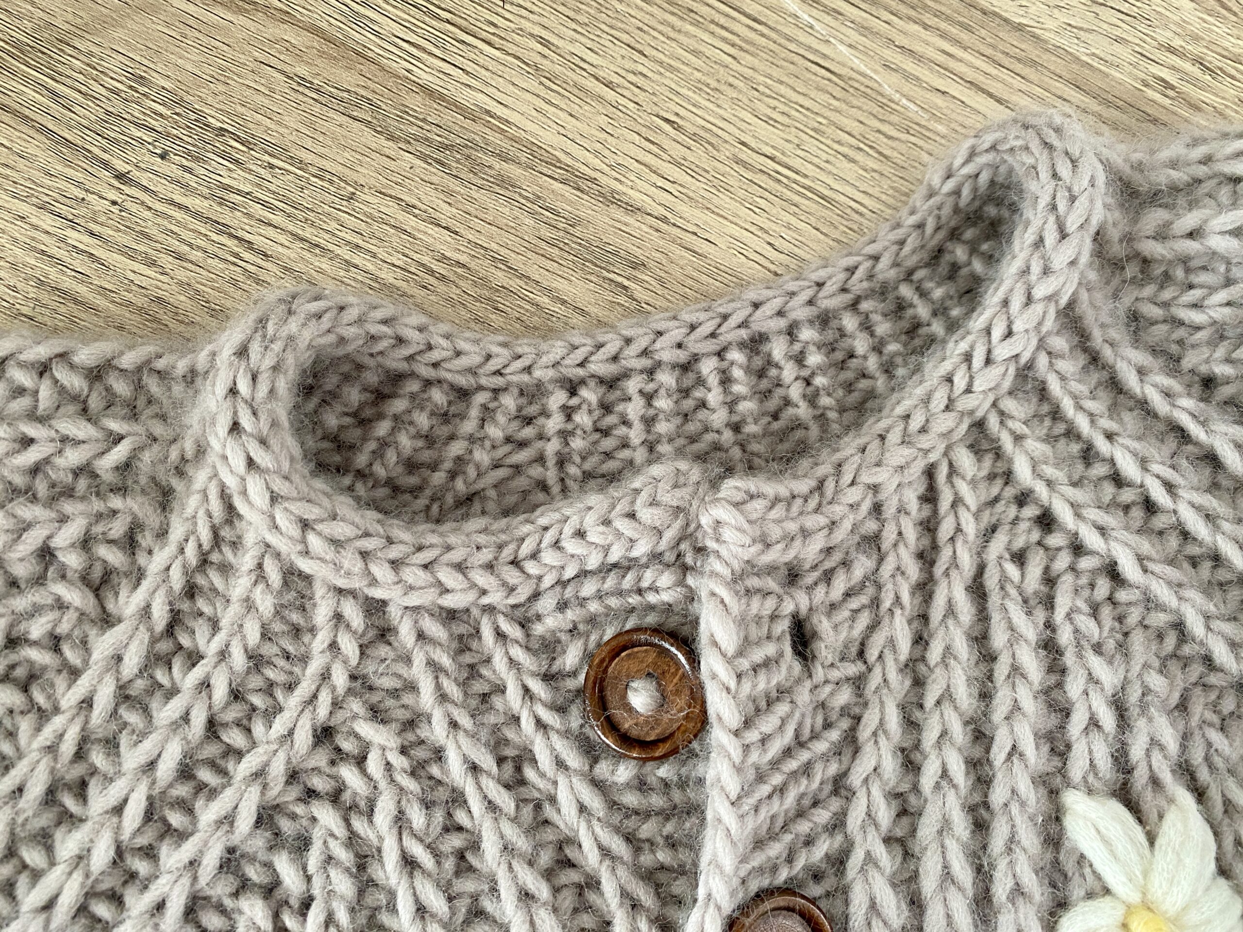 A detailed view of the neckline of the Fluffy Daisy Cardigan, highlighting the ribbed texture and a wooden button closure.