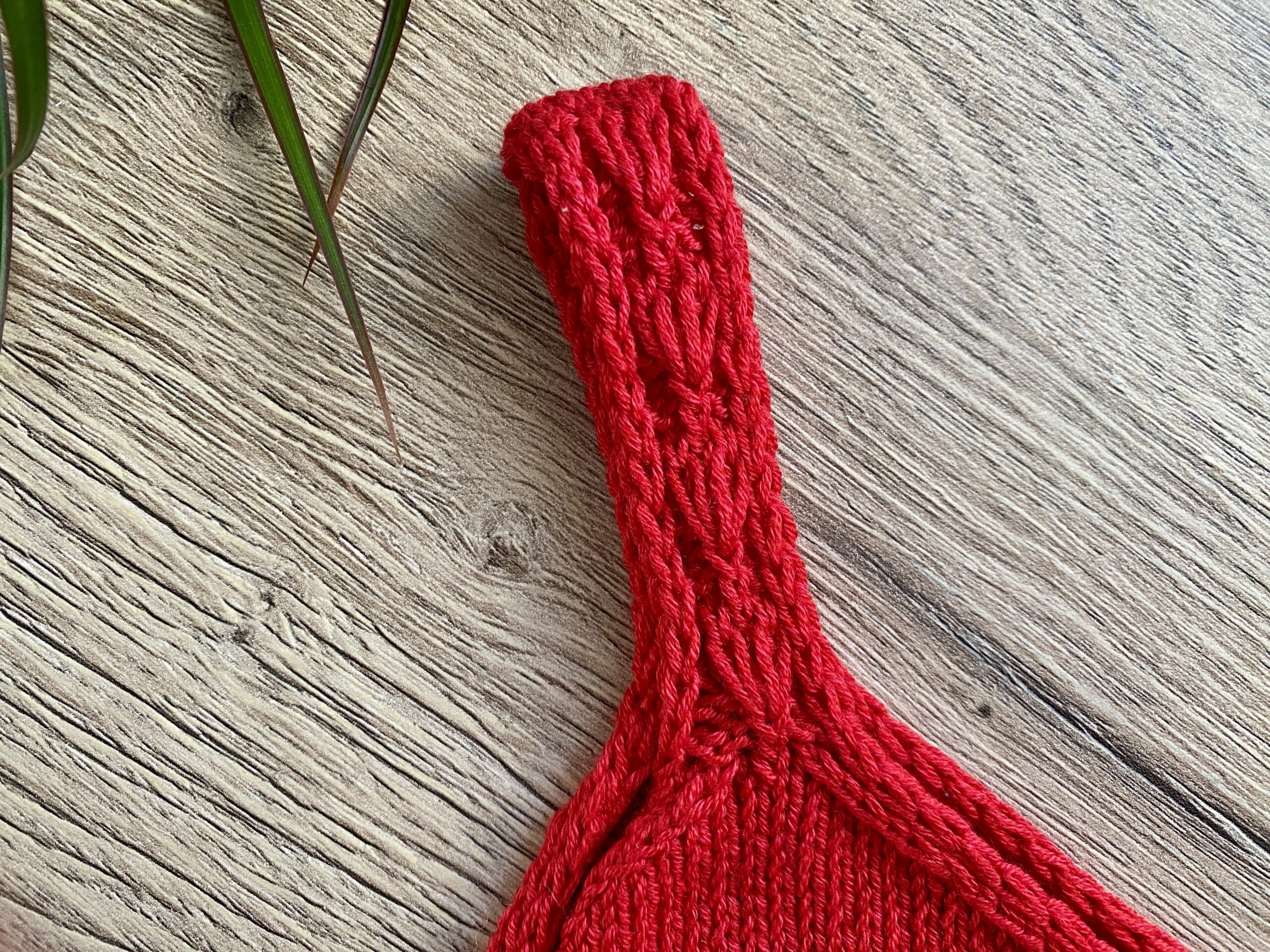 A detailed view of one of the straps of the Ginkgo Biloba Top, highlighting the neat knit texture in vibrant red yarn, laid flat on a wooden surface.