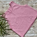 A knitted Minimalist Tank Top in soft pink yarn, displayed with two skeins of "Linea Pura COTTON" yarn and a printed pattern sheet featuring the design. The setup is laid on a rustic wooden surface.