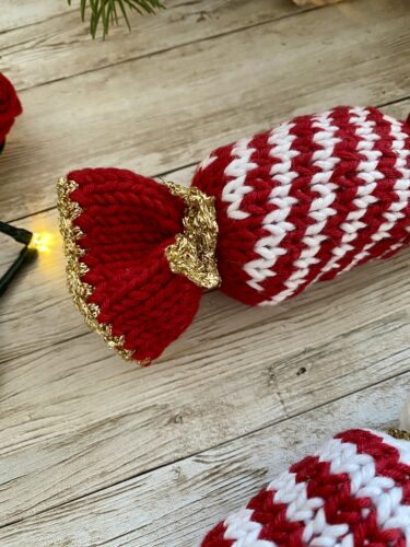 A detailed view of the end of a red knitted Christmas Caramel, showcasing the gold trim and bow detail, with a rustic wooden background.