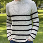 A front view of the Vine Pullover, showcasing its classic cream and black striped design with a crew neckline and a relaxed fit. The pullover is worn with blue jeans in a sunny park setting.