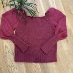 Red knitted sweater lying on a wooden floor with a green plant