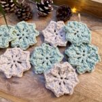 Wooden tray with crocheted facial scrubbies in green and beige, styled with pinecones and fairy lights.