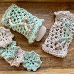 A wooden tray with crocheted flower motifs in green and beige on the left, and two crocheted soap pouches with drawstrings and wooden beads in the center and right.