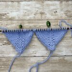 Close-up of knitted swatch on wooden knitting needles, in blue yarn, showing knitting techniques.