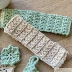 A flat lay of handmade crochet items in soft mint green and cream colors, displayed on a wooden surface. The collection includes two drawstring pouches with star stitch patterns, two rectangular washcloths, and several small star-shaped motifs. A small white pot with a green succulent is placed in the top right corner, adding a decorative touch to the arrangement.