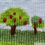 A knitted square using the intarsia technique, depicting a landscape with green hills, two trees with red apples, white clouds, and a purple butterfly against a light blue sky.