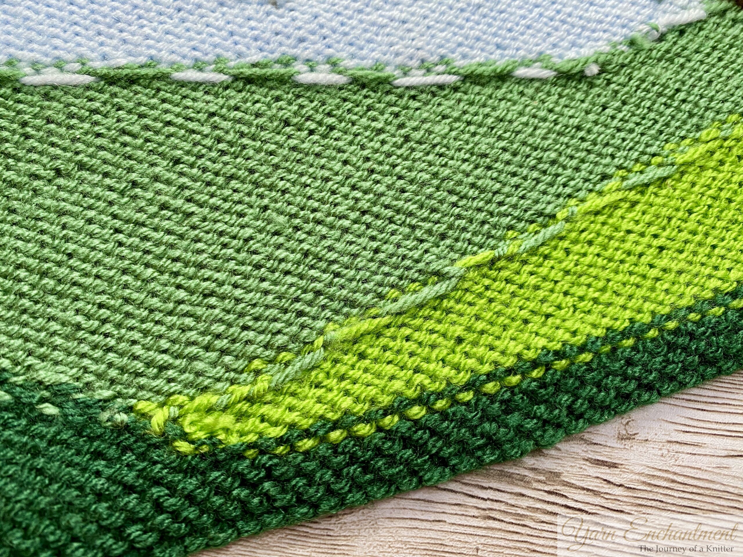 A close-up of a knitted fabric with green shades, showing detailed stitching and texture.