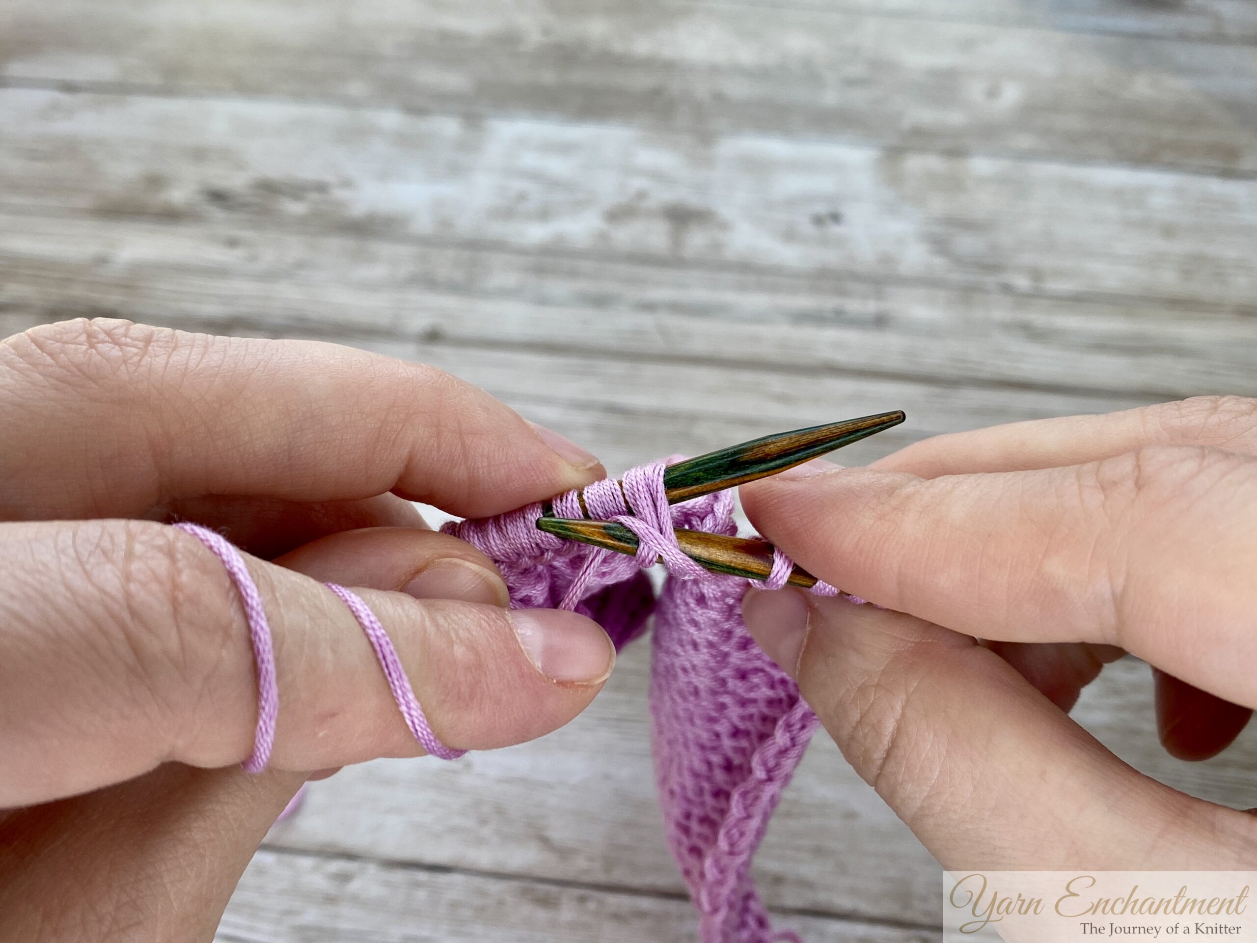 Hands holding wooden knitting needles with light pink yarn, demonstrating the 'purl 2 together' decrease technique.