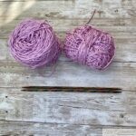 Two pink yarn skeins and wooden knitting needles on a wooden surface, ready for a knitting project.