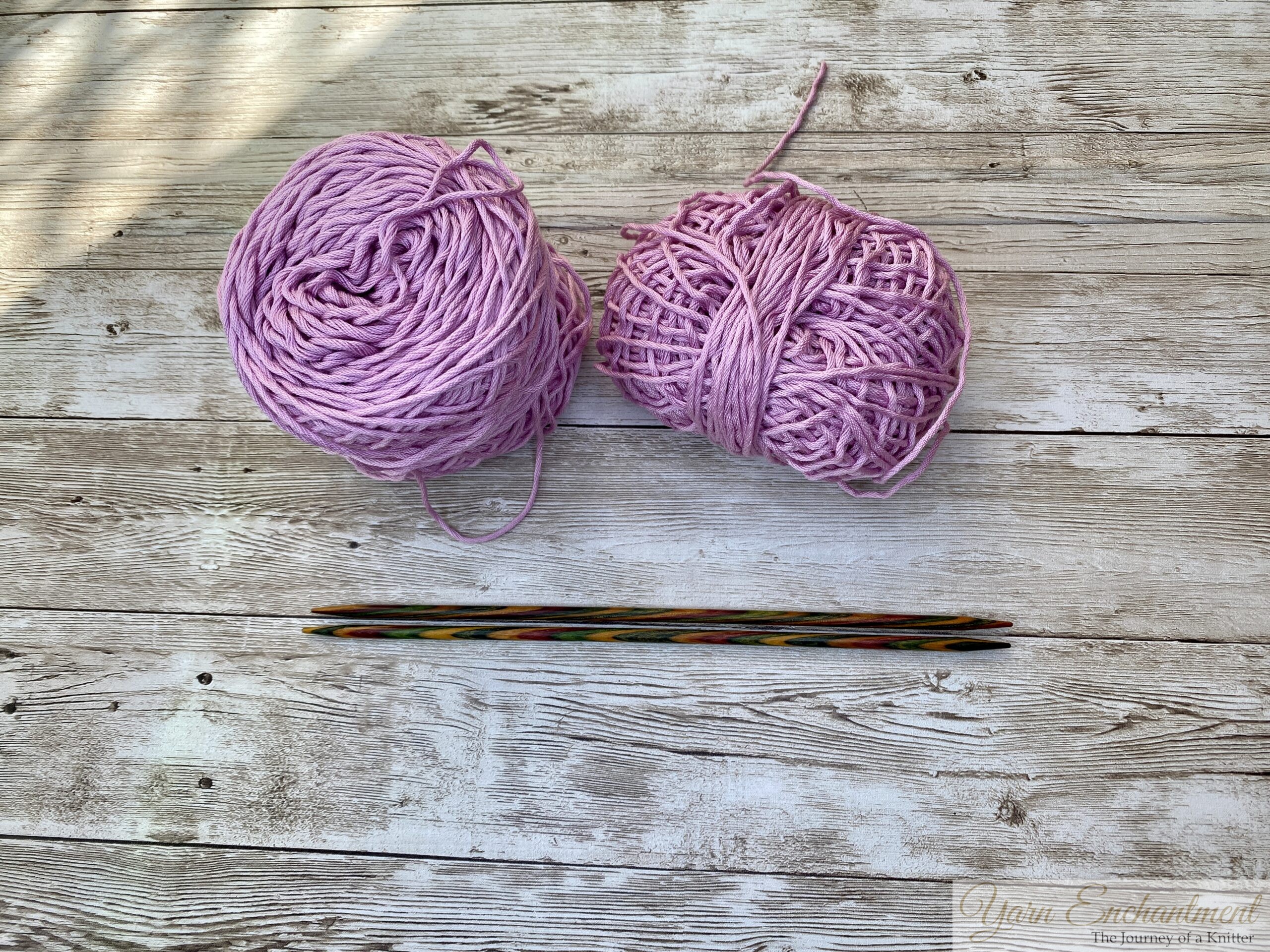 Two pink yarn skeins and wooden knitting needles on a wooden surface, ready for a knitting project.