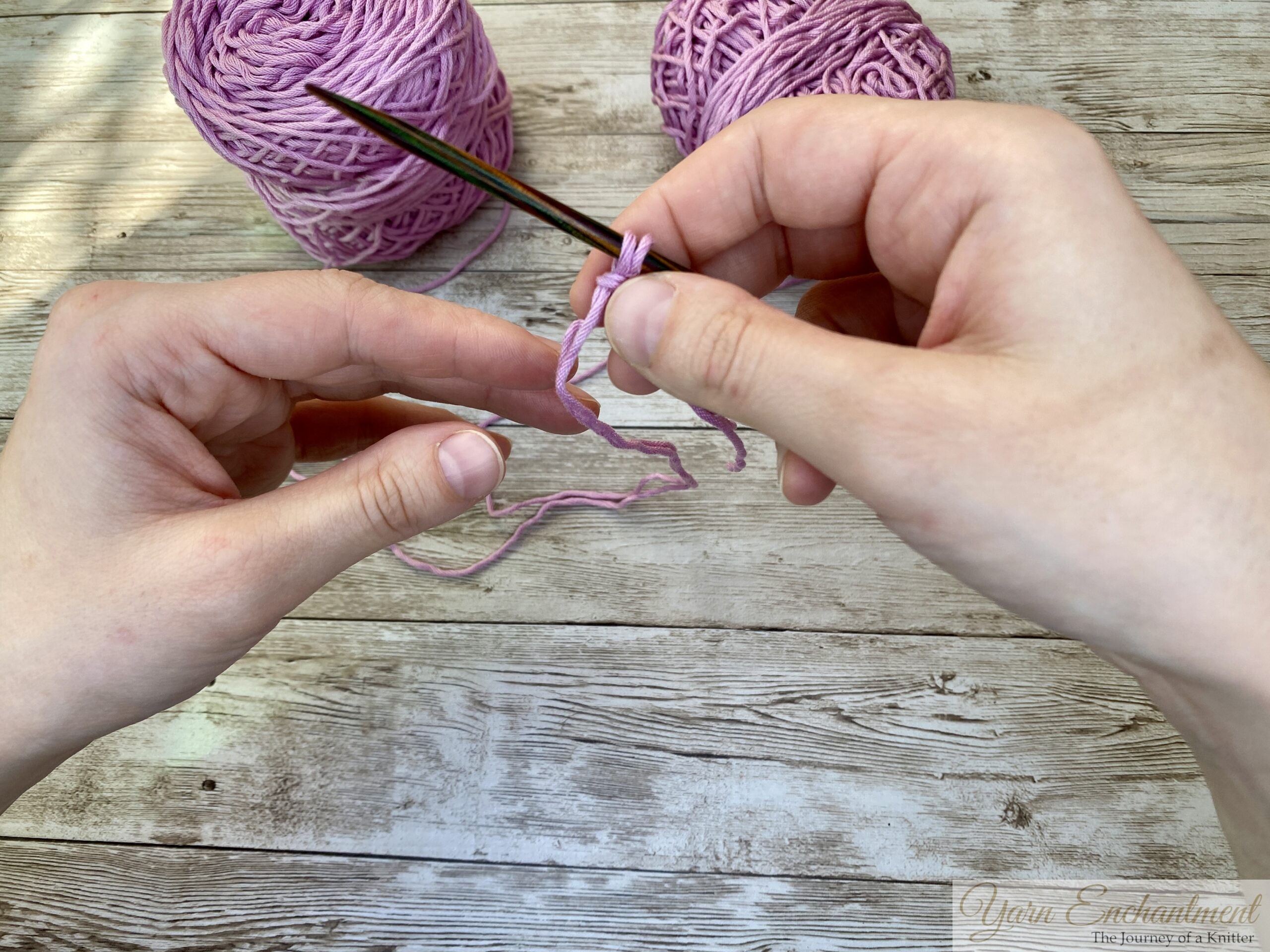 Hands holding knitting needles and pink yarn, demonstrating the long-tail cast-on technique