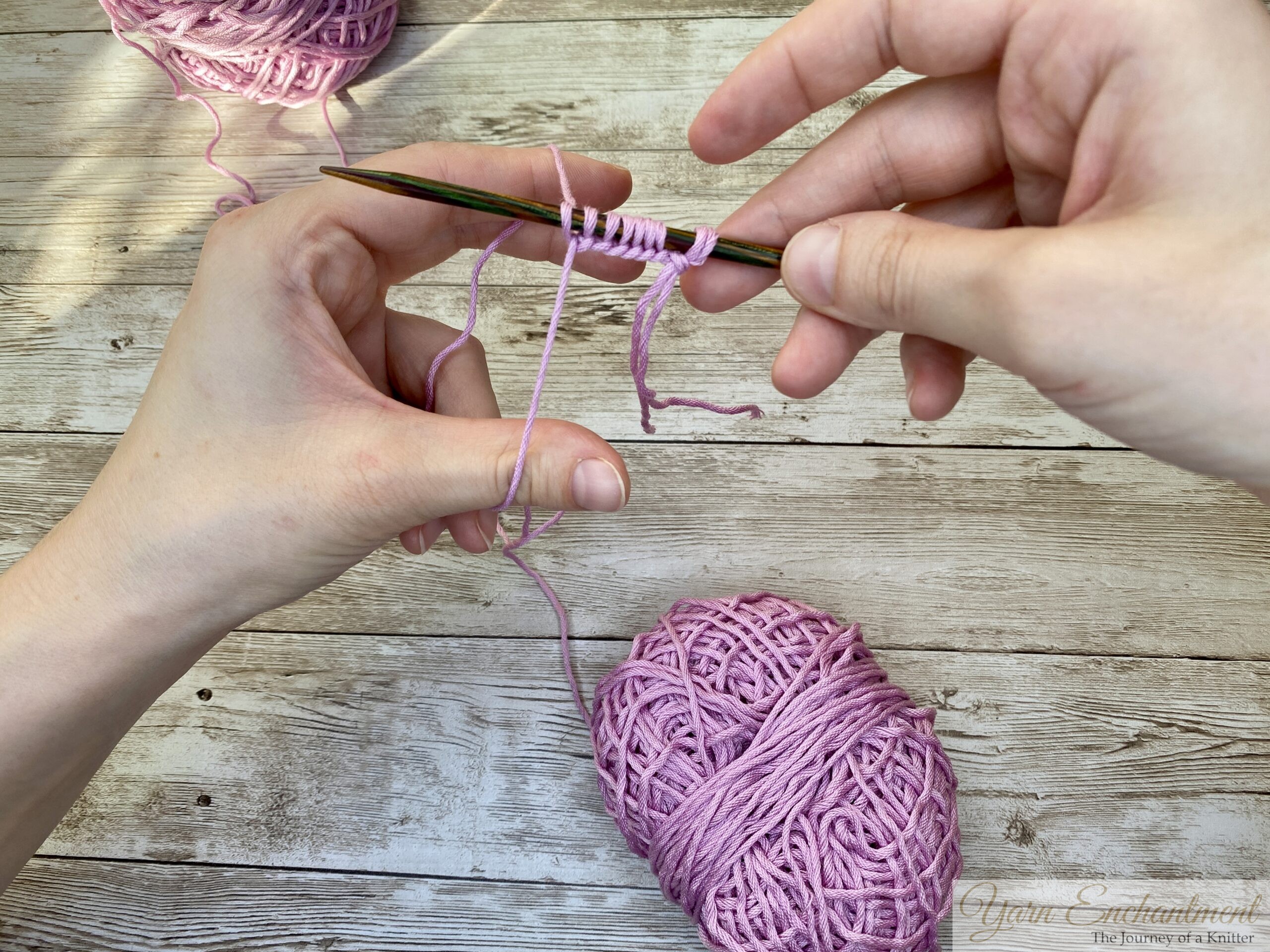 Knitting needles with pink yarn, showing completed cast-on stitches using the long-tail method.