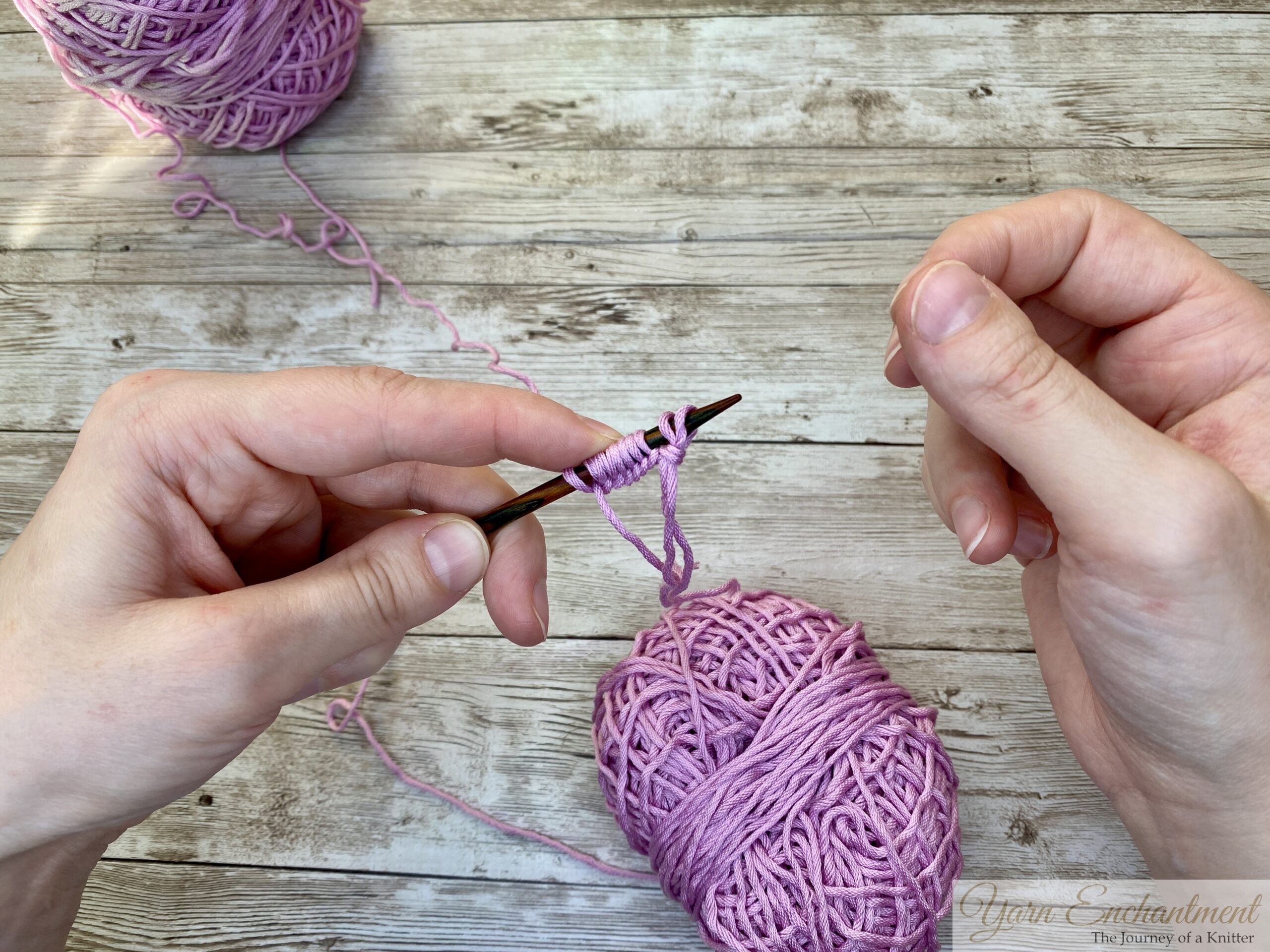 Knitting needles with pink yarn, showing the slip knot at the end