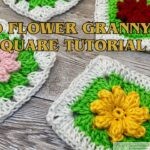 An angled view of four beautifully crocheted 3D flower granny squares with flower centers in blue, red, pink, and yellow, surrounded by green petals and white borders, on a rustic wooden surface. Writen in yellow is 3D Flower Granny Square Tutorial