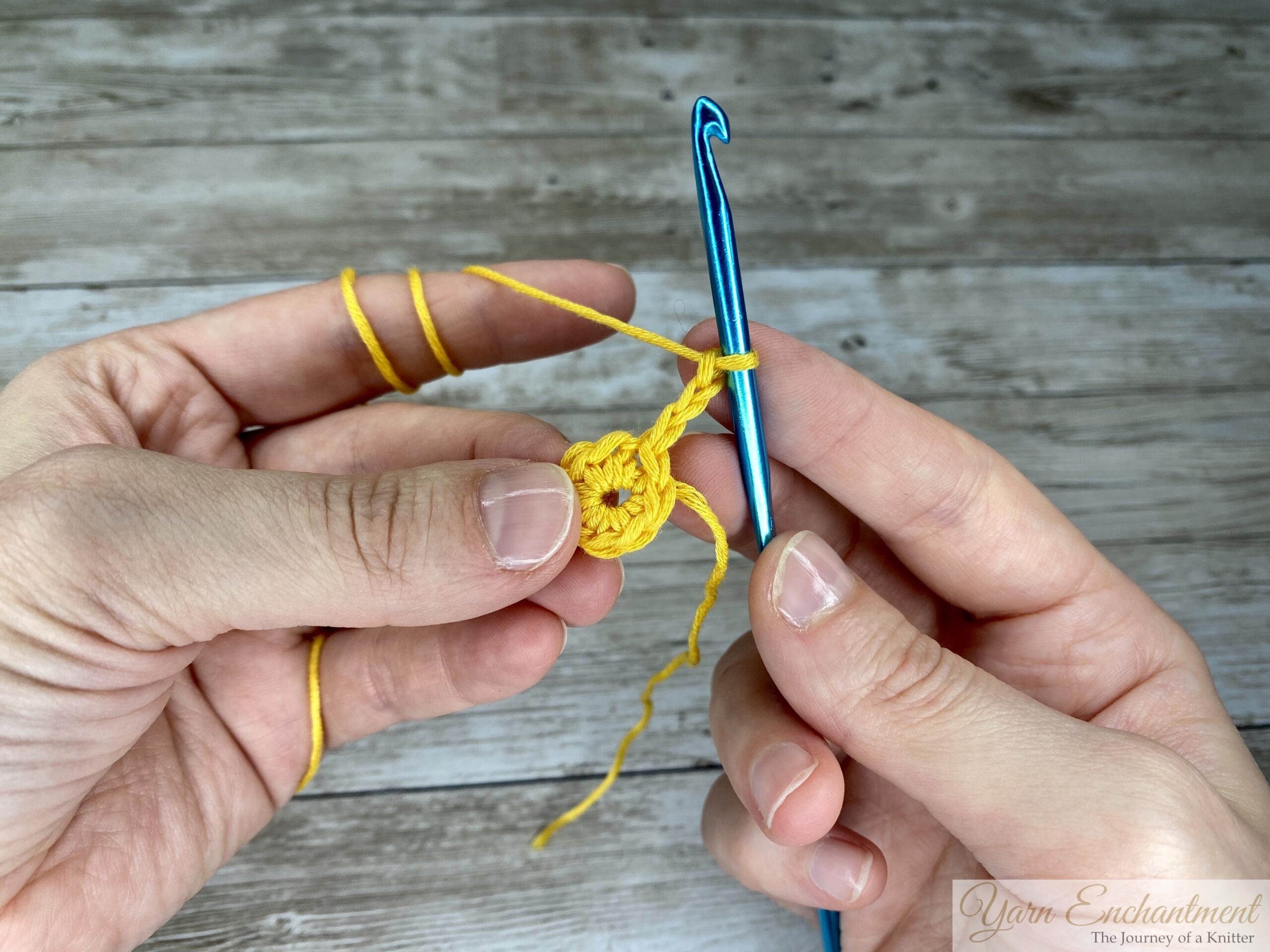 Close-up of a crochet hook chaining 3 stitches with a yellow yarn.