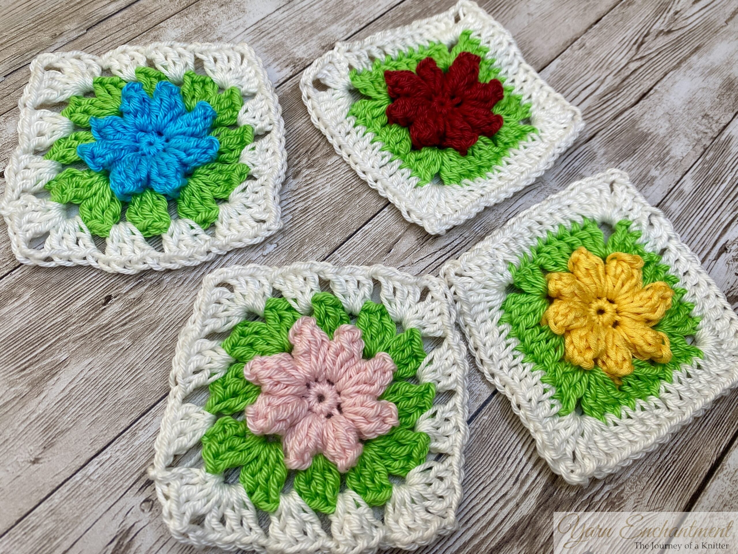 Four colorful 3D flower granny squares arranged together on a wooden surface, featuring flowers in pink, yellow, red, and blue, all framed by green petals and white borders
