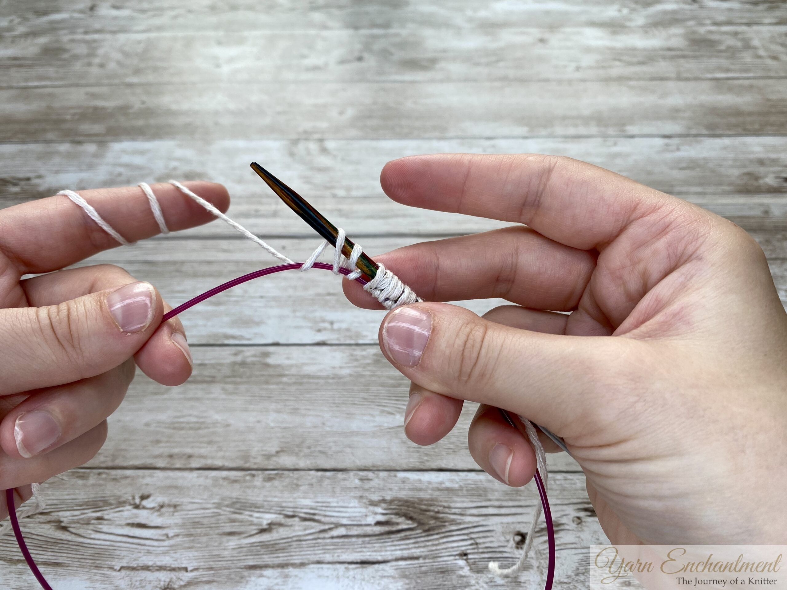 Progress on the provisional cast-on. The wooden needle holds several white yarn loops, while the pink cable underneath secures the provisional stitches for future use.