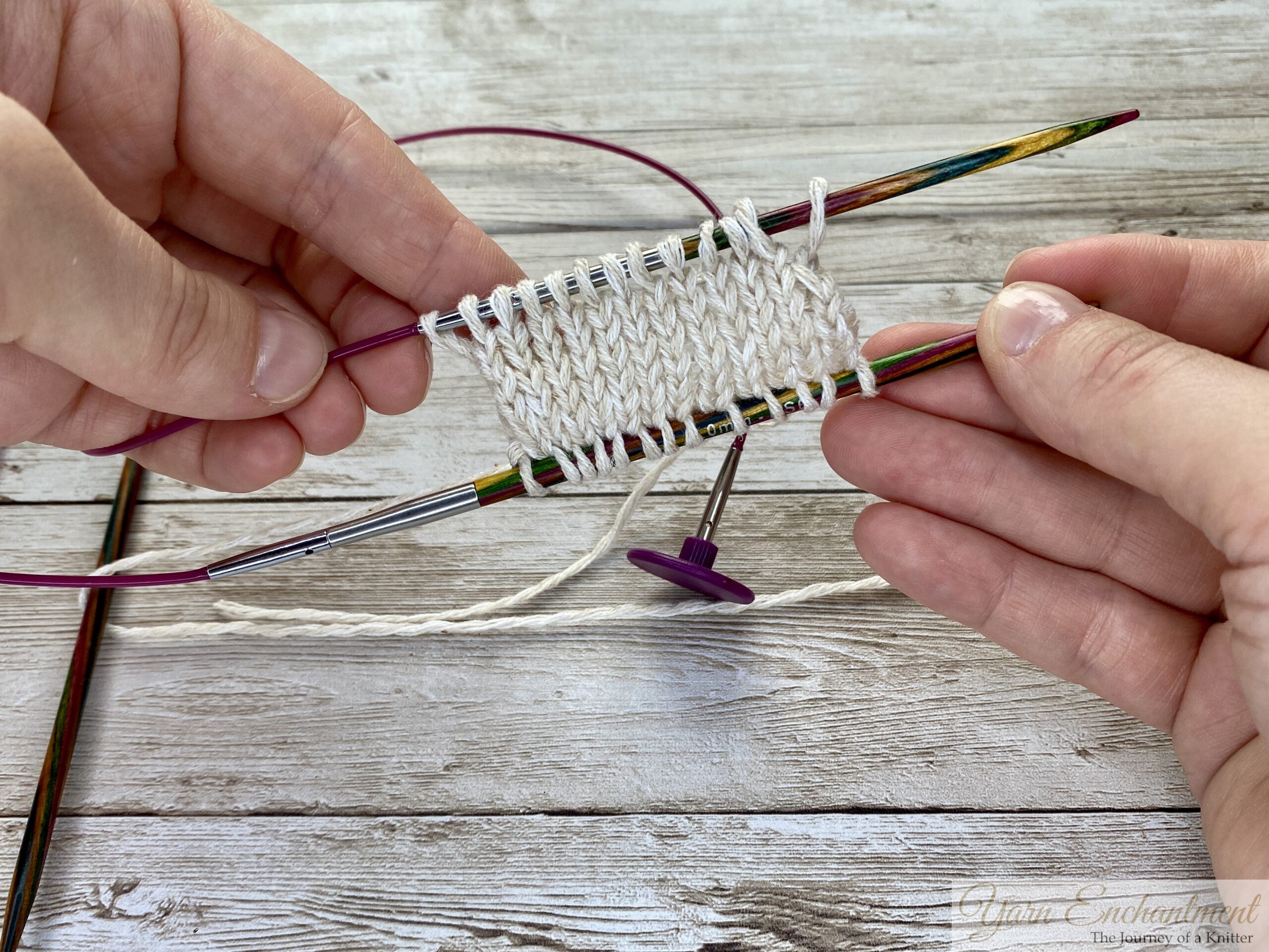 Two hands holding the project. The wooden needles are actively knitting. The swatch is shown in progress, demonstrating how the technique maintains the stitches.