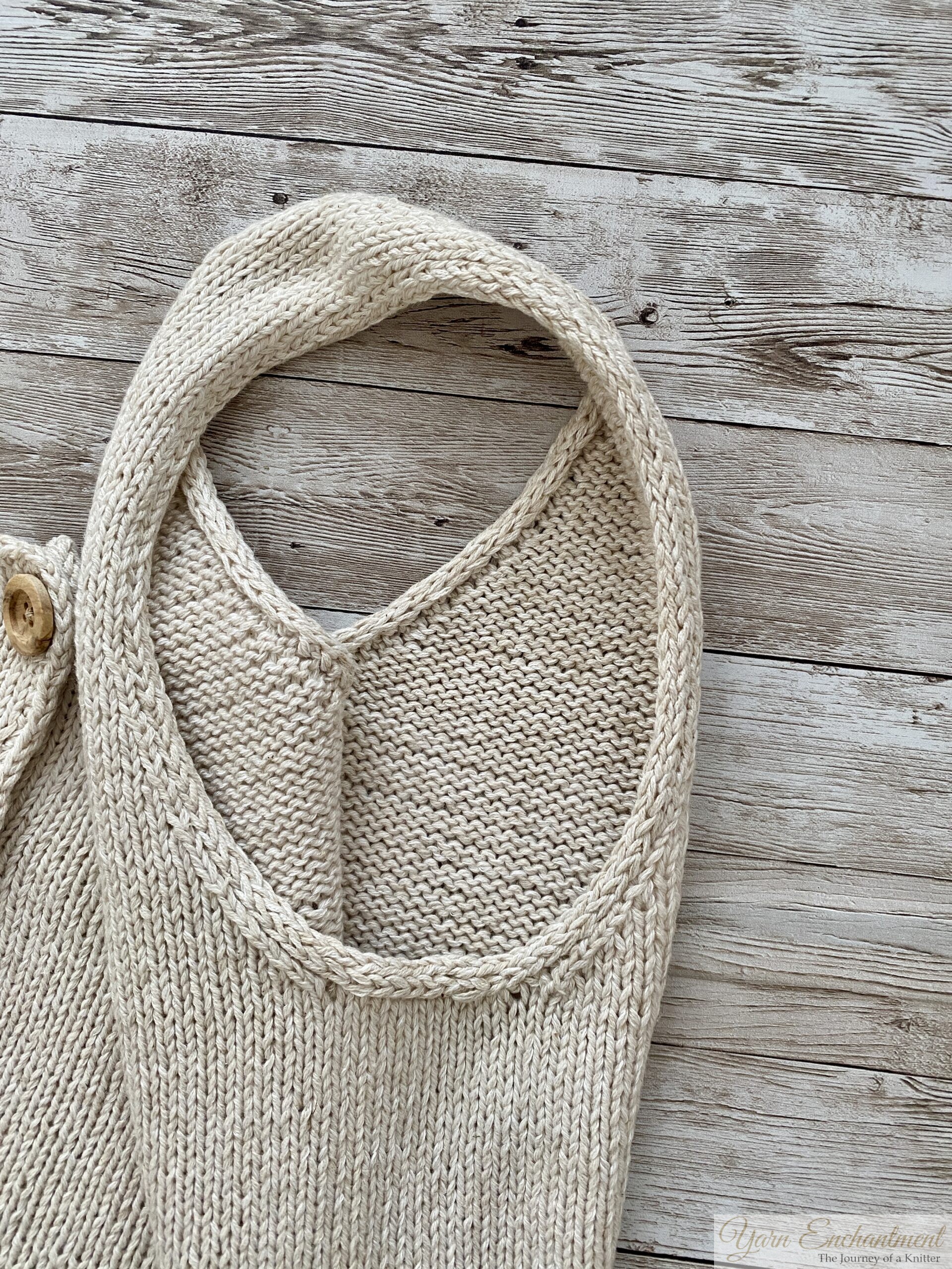 A close-up of the neckline and armholes of a beige knitted garment, showcasing the clean, even edging and smooth stockinette stitch. The wooden background highlights the texture of the fabric.