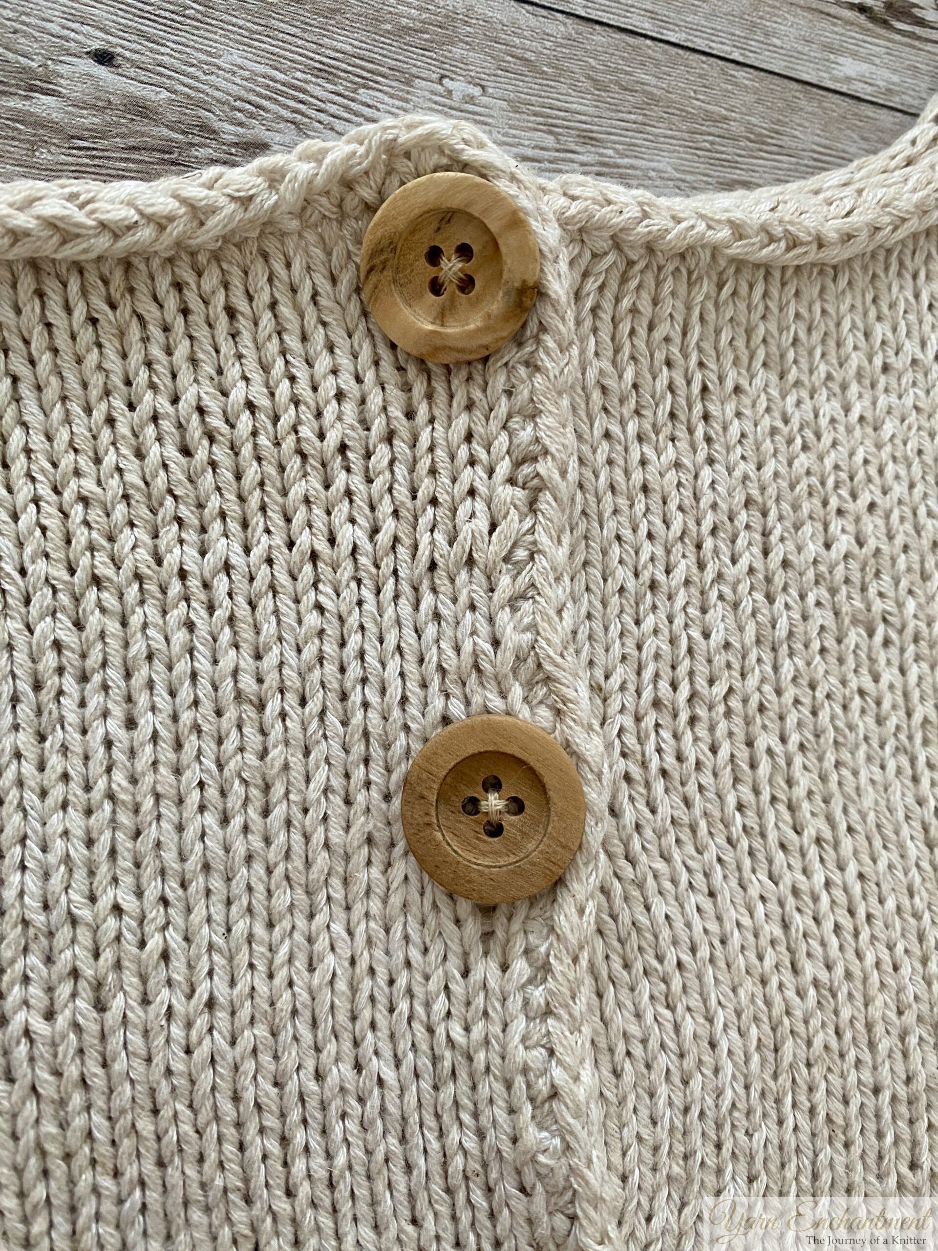 A detailed view of two wooden buttons on a beige knitted garment, showcasing the neat buttonhole edging and the smooth, even stitching of the fabric.