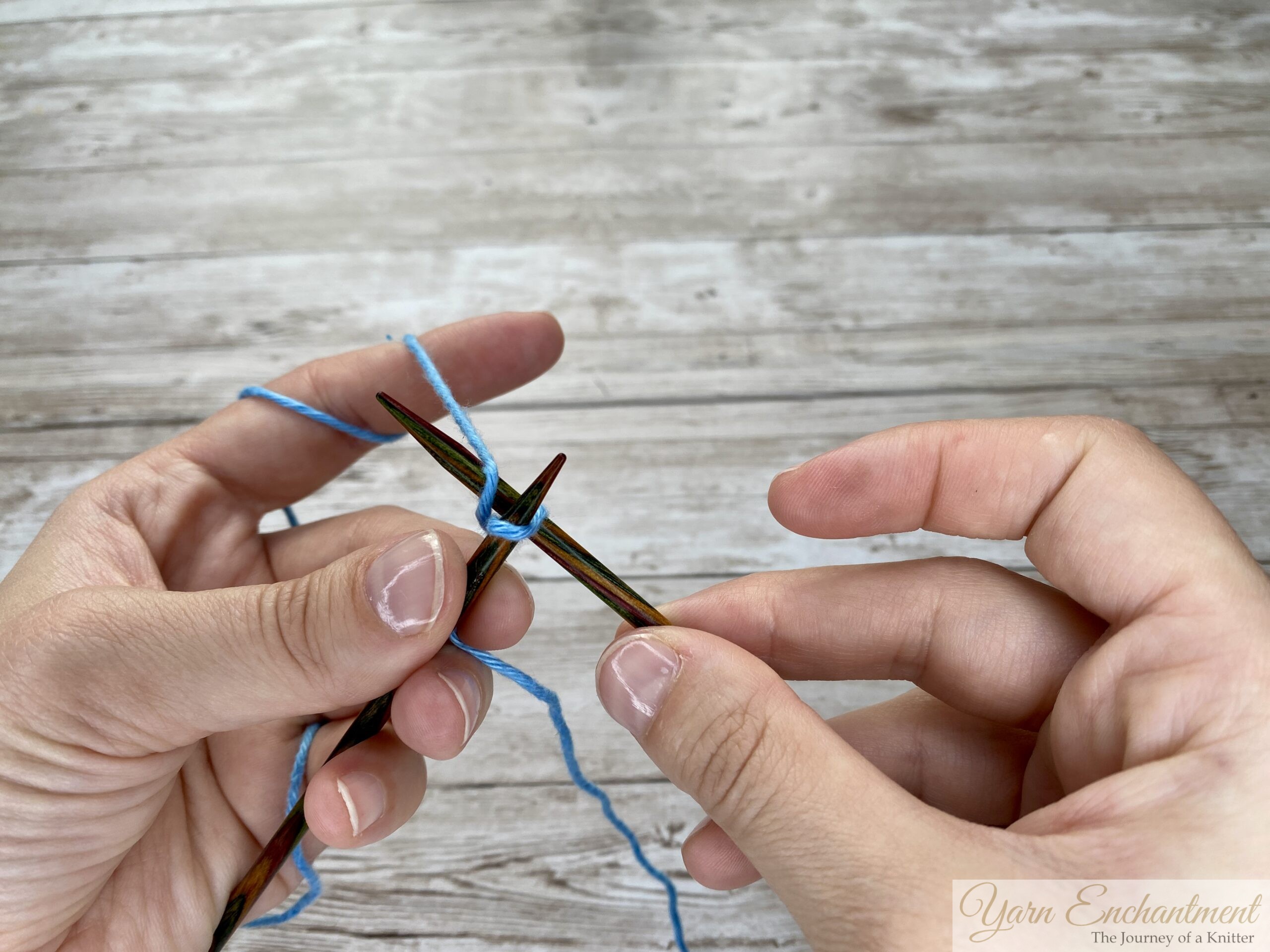Knitting needle with a secured blue loop as hands prepare to continue the knitted cast-on process.