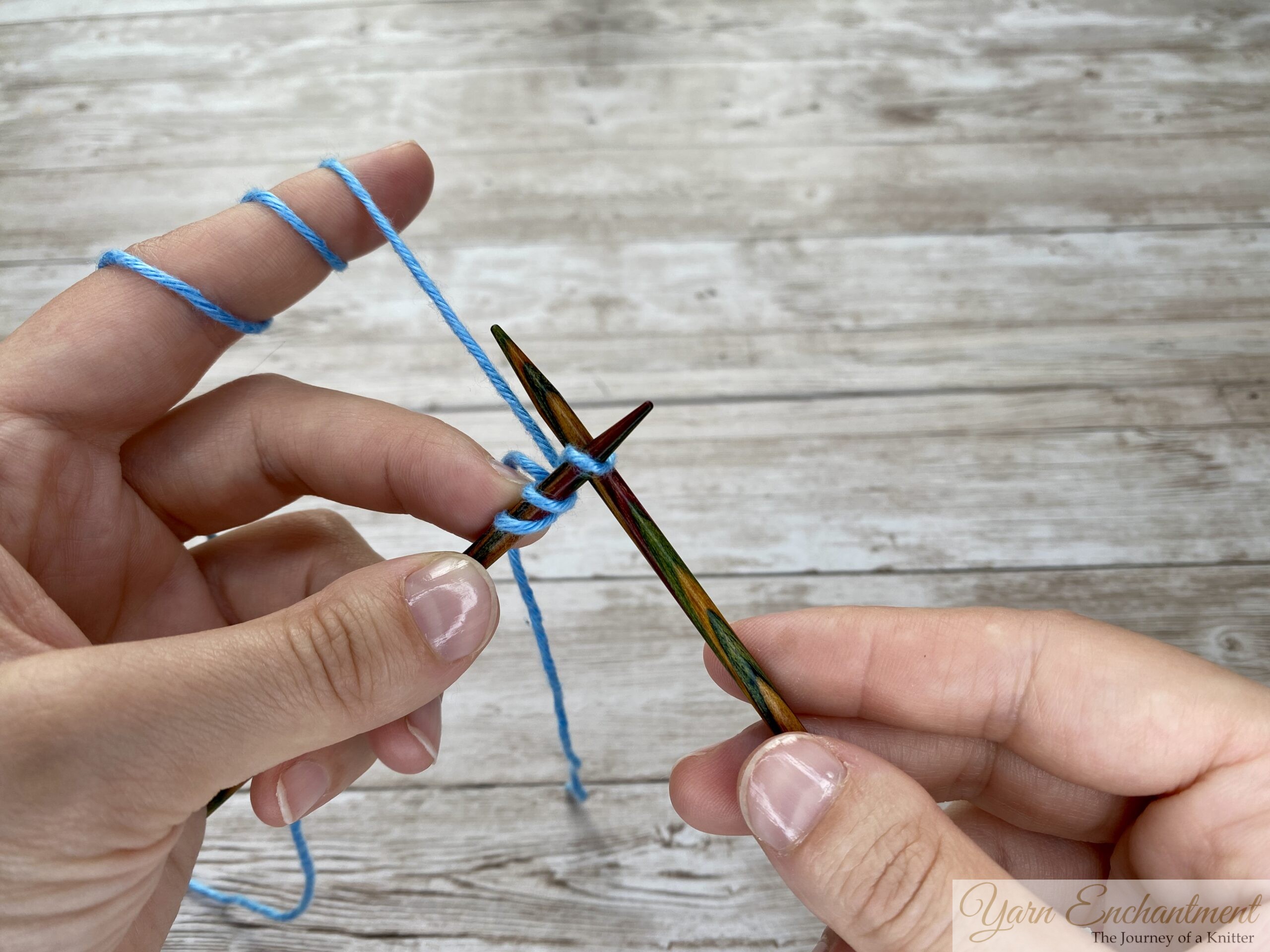 Knitting needles positioned as stitches are formed with blue yarn during a knitted cast-on.