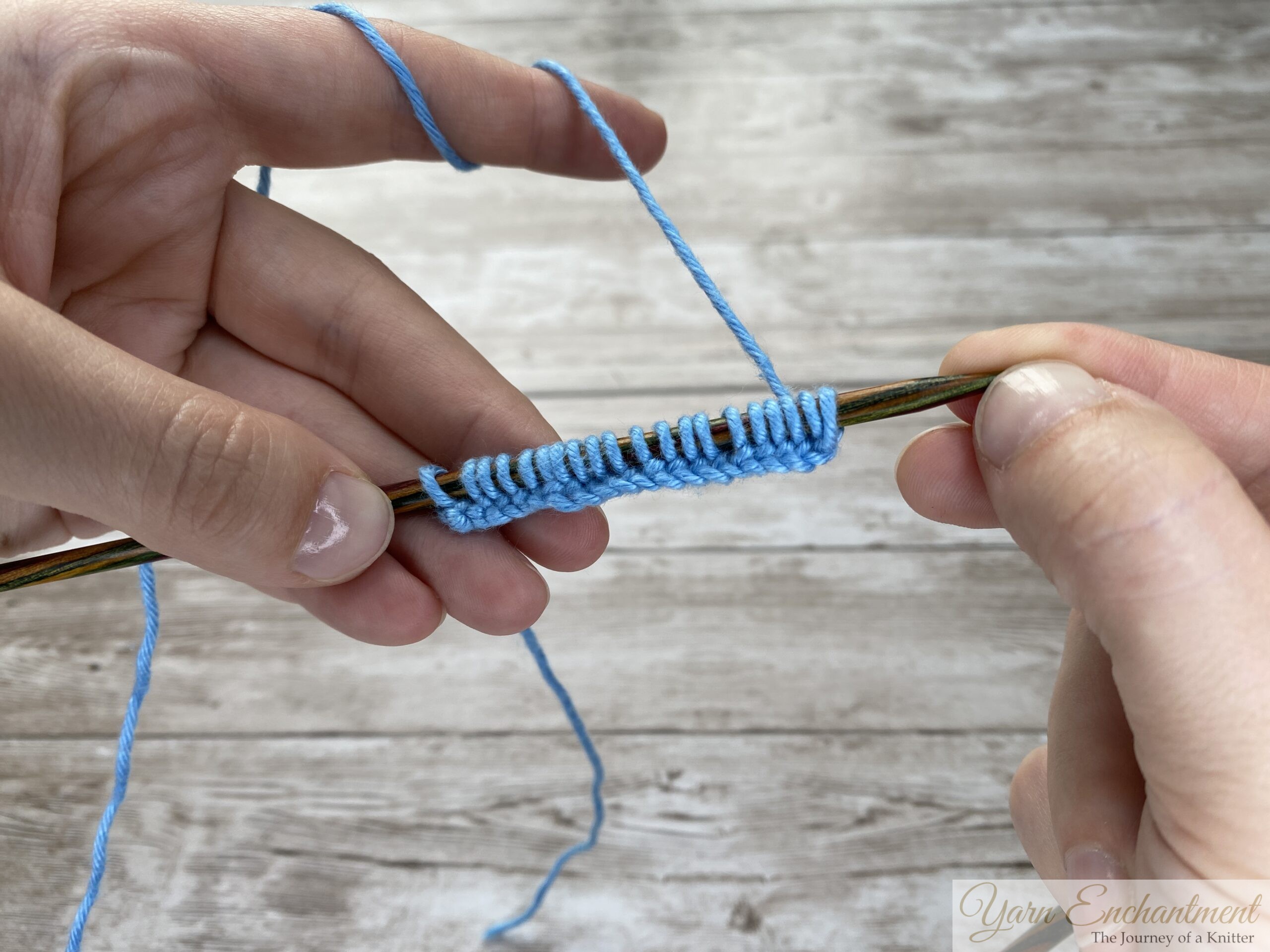 Completed row of evenly spaced blue cast-on stitches on a wooden knitting needle