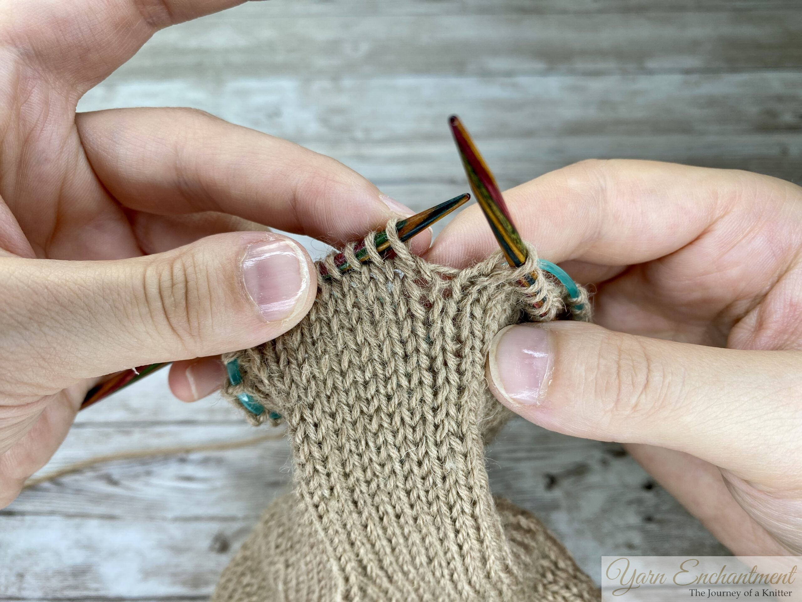 Hands holding colorful knitting needles after transferring the last repaired stitch from the crochet hook back onto the left needle, with all stitches correctly aligned and ready to continue knitting the row.