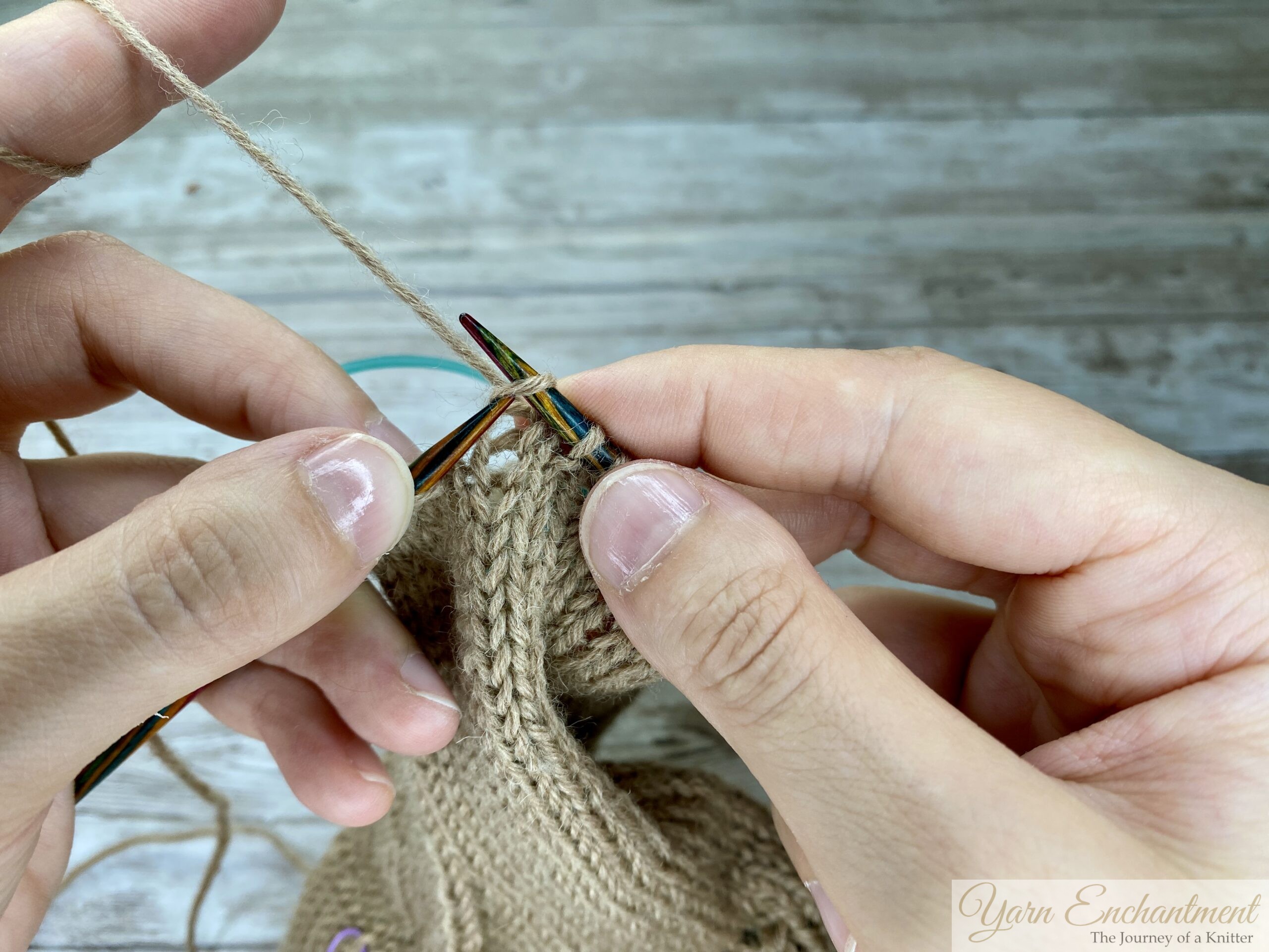 Hands returning the repaired stitch onto the left knitting needle, with all stitches aligned and ready to continue knitting.