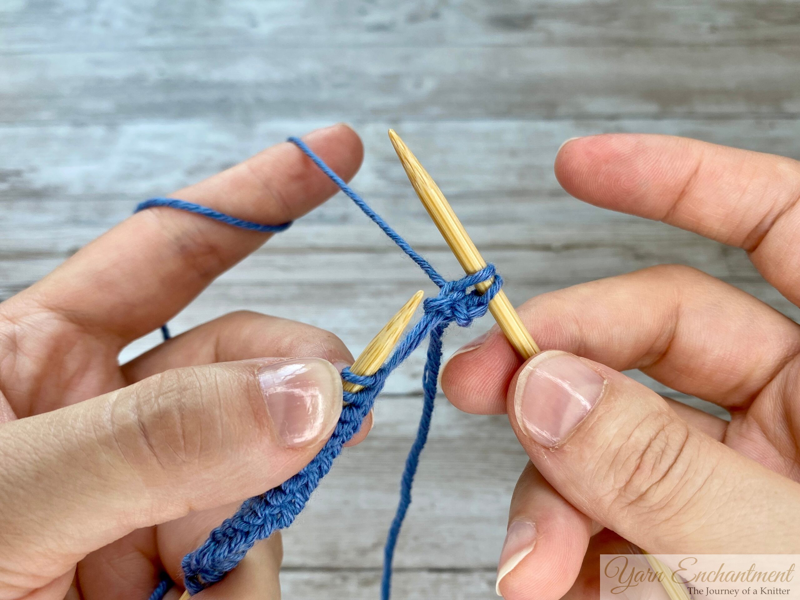 Hands showing the completion of the knit stitch, as the right needle carries a new loop and the old stitch has been slipped off the left needle.