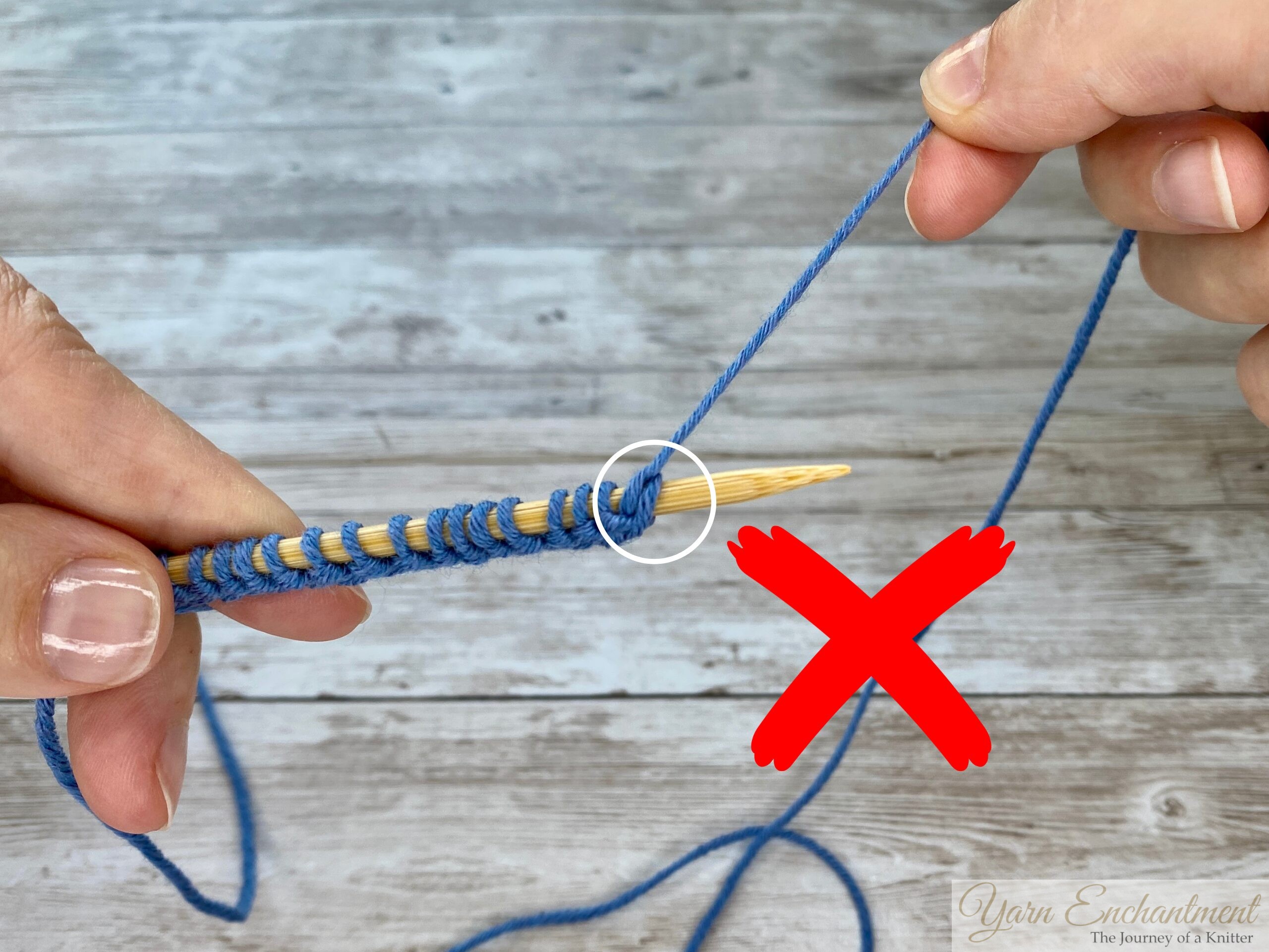 Hands displaying the completed cast-on row of blue stitches along a bamboo knitting needle, with the right needle empty and ready to continue the knitting process.