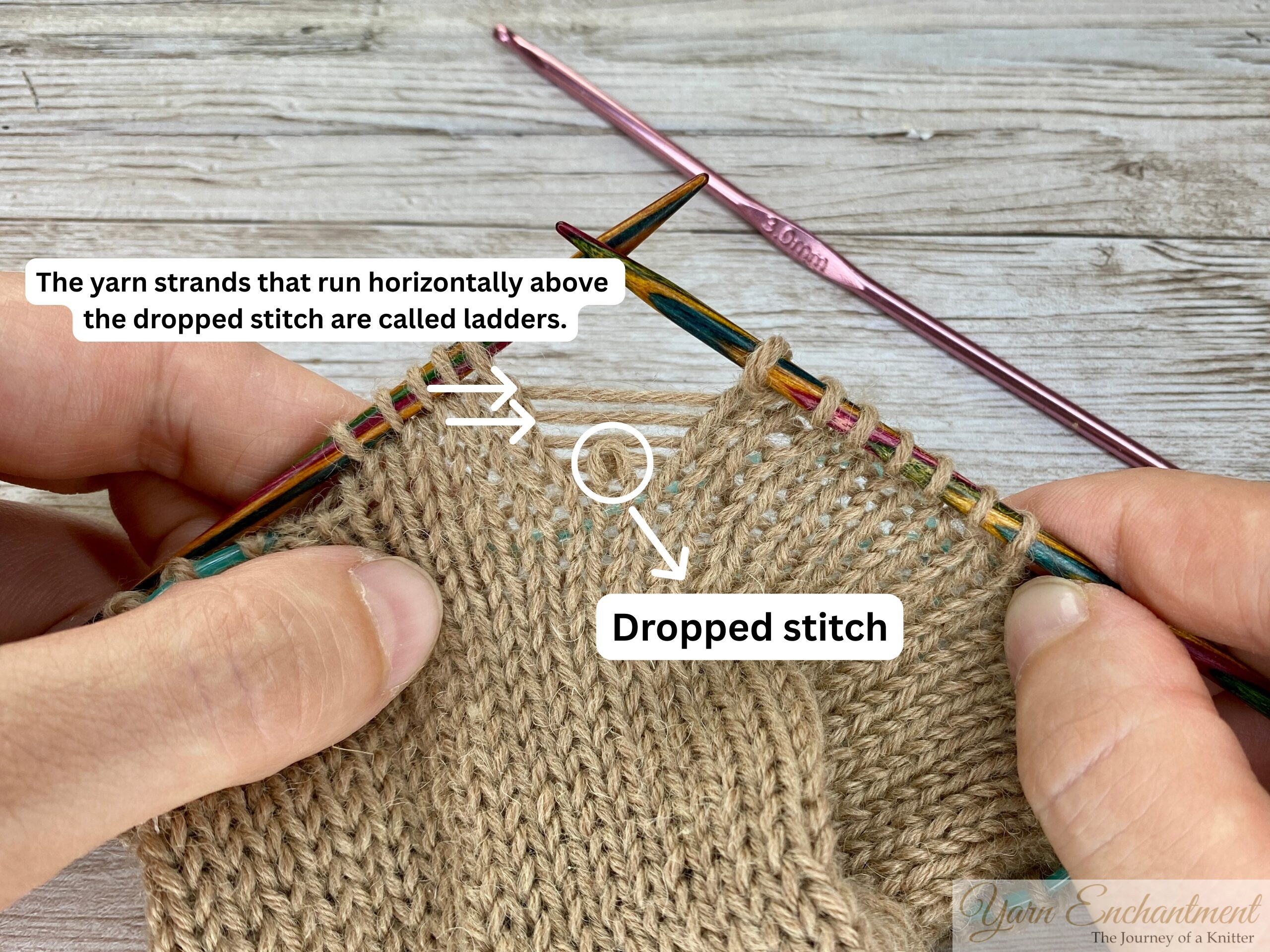 Hands holding colorful knitting needles, demonstrating how to fix a dropped stitch in beige stockinette fabric. Several horizontal yarn strands, called ladders, are visible above the dropped stitch.