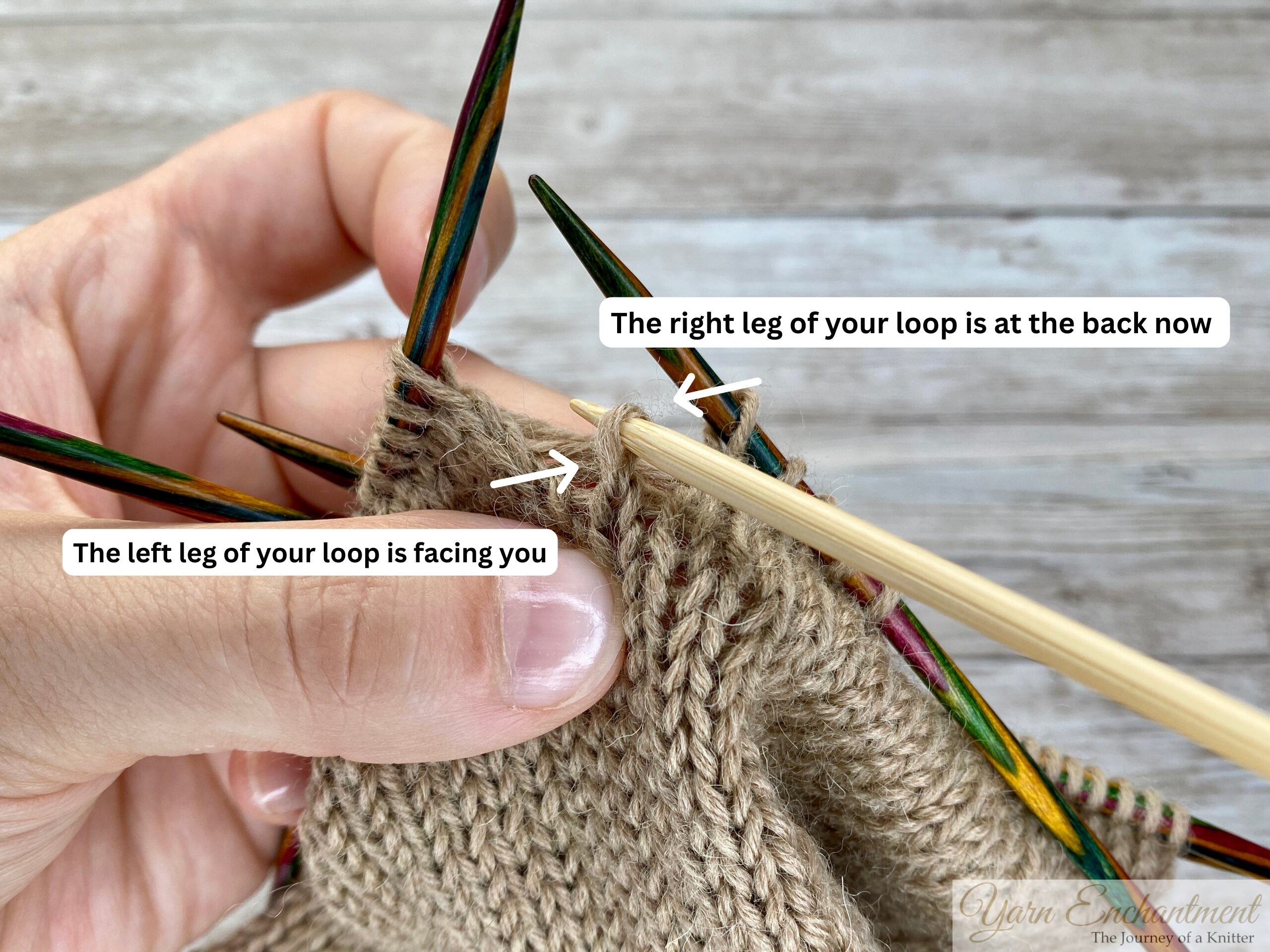 Hands holding colorful double-pointed knitting needles, demonstrating how to fix a dropped stitch in beige stockinette fabric. The left leg of the loop is facing the viewer, while the right leg is at the back, illustrating the correct stitch orientation for repair.