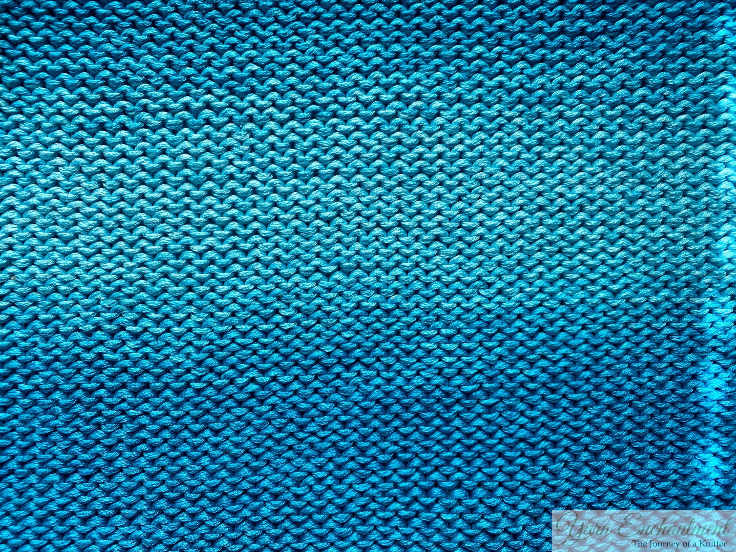 Bright blue close-up of a hand-knitted garter stitch fabric, showing its textured, bumpy rows in clear detail.